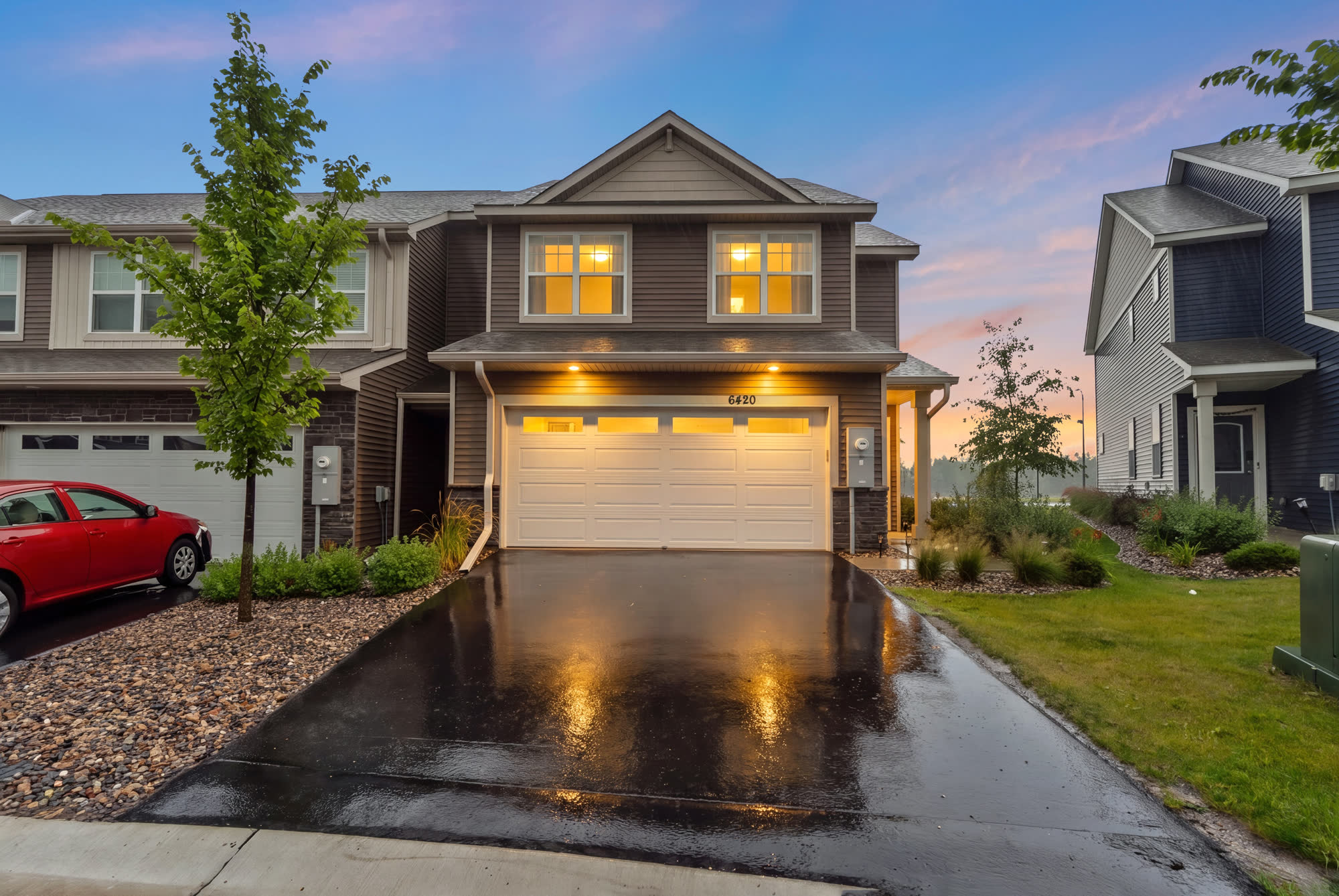 Twilight exterior of a Minnesota townhome, windows lit and the driveway still wet from rain
